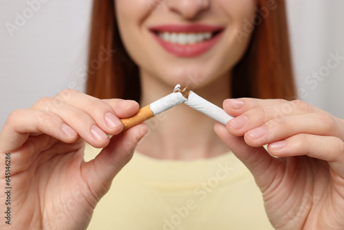 Stop smoking concept. Woman breaking cigarette on light gray background  closeup