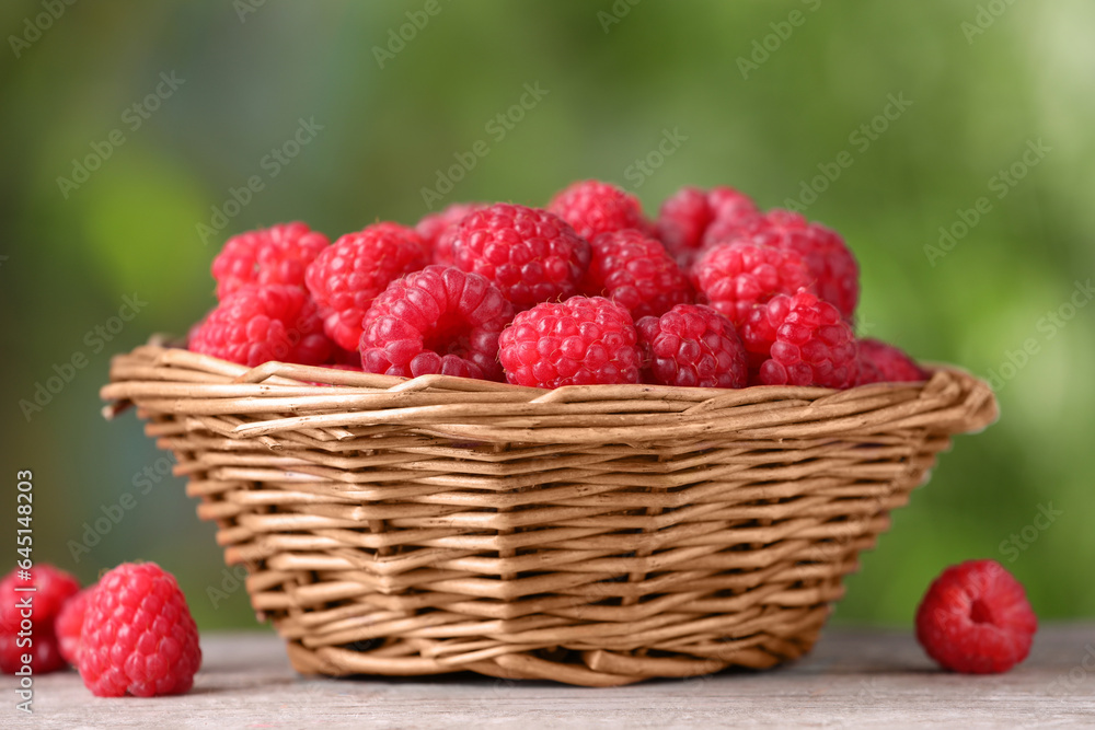 Wicker basket with tasty ripe raspberries on wooden table against blurred green background, closeup Wicker basket with tasty ripe raspberries on wooden table against blurred green background, closeup