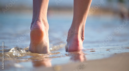 Close up of female feet walking barefoot on white grainy sand of golden beach on blue ocean water background © bilanol