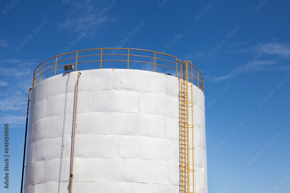 Detail of white reservoir with yellow ladder and blue sky in the background. Detail of white reservoir with yellow ladder and blue sky in the background.