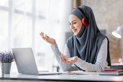 Online Education For Muslim Asian Women. Happy Arabic Girl In Headscarf And Headset Studying With Laptop At Home, Taking Notes While Watching Webinar