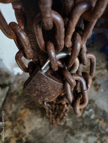 a photo of an old and rusty chain and padlock, reddish brown, hanging from a wooden pole.