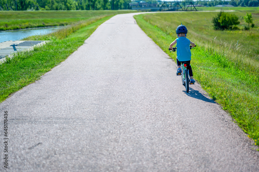 Fototapeta premium Caucasian boy wearing a helmet while riding a bike down a paved park path 