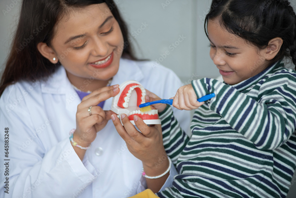 Dentist showing a jaw model to a little girl and suggest the correct