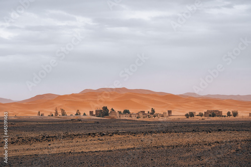 Houses and palm trees in front of the big Sahara Desert in Merzouga, Morocco