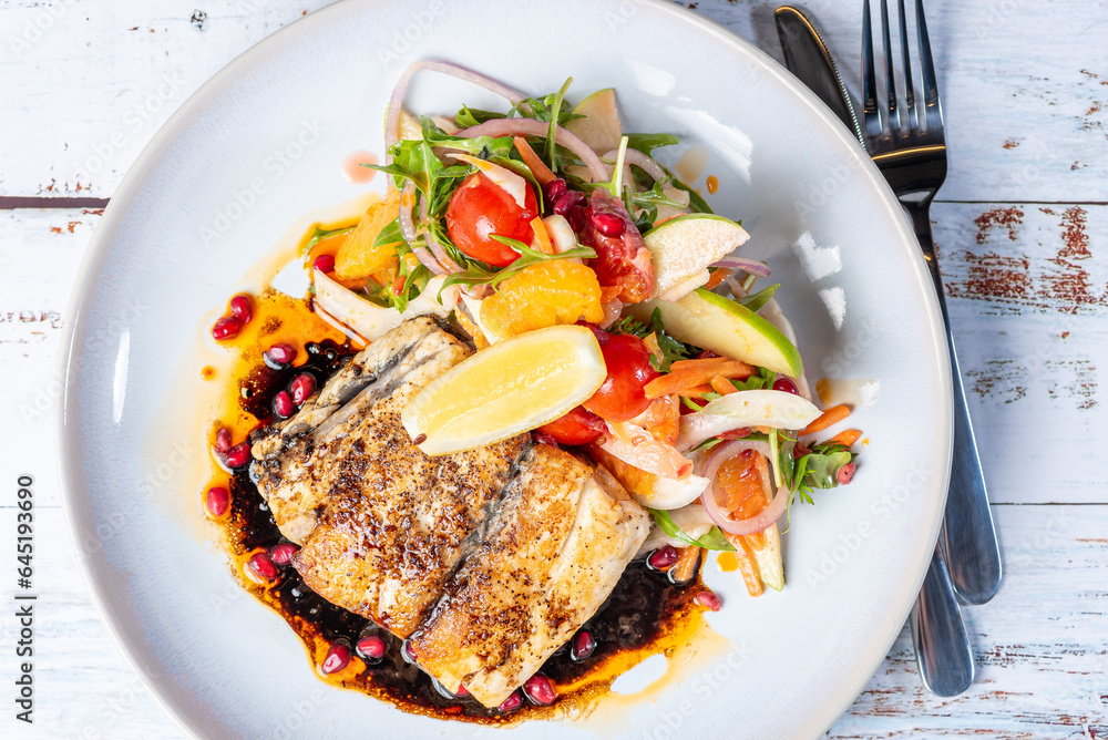 Grilled Barramundi with a side of salad, served on a white round plate with knife and fork.