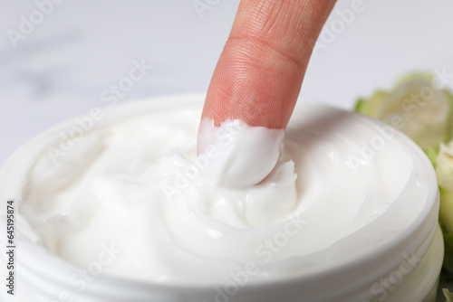 Jar with cream and finger on marble background, close up