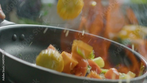 Close-up shot in slow motion of tossing flambe vegetables in a frying pan during cooking in the kitchen photo