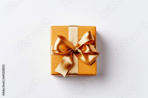 Mustard yellow gift box with gold satin ribbon bow isolated on white background, top view, celebrated Thanksgiving or birthday background.