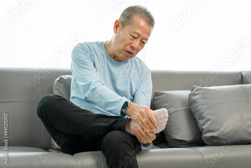 Photography Senior Elderly Asian man in blue shirt suffering from intense foot and ankle pain on the sofa