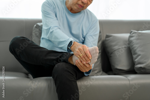 Εκτύπωση καμβά Senior Elderly Asian man in blue shirt suffering from intense foot and ankle pain on the sofa