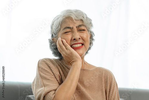 Elderly asian woman sitting on the couch, tooth decay, toothache.
