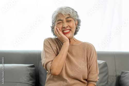 Elderly asian woman sitting on the couch, tooth decay, toothache.