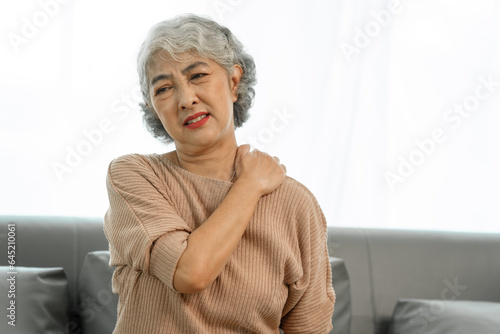 Elderly asian woman sitting on the couch, shouder pain.