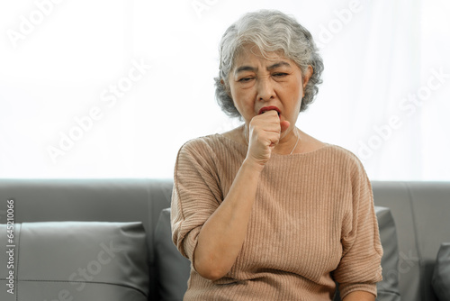 Elderly asian woman sitting on the couch, Cough, sore throat.
