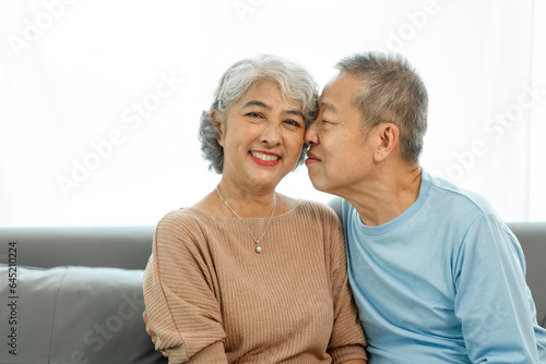 Affectionate senior Asian couple sharing warm embrace on the sofa, celebrating their enduring love and togetherness. Elderly husband and wife happy family © makibestphoto