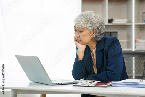 Mature businesswoman at her desk, overwhelmed by stress, feeling the weight of failure, and suffering from a headache, Stressful workday, Overwhelmed at work, Corporate crisis