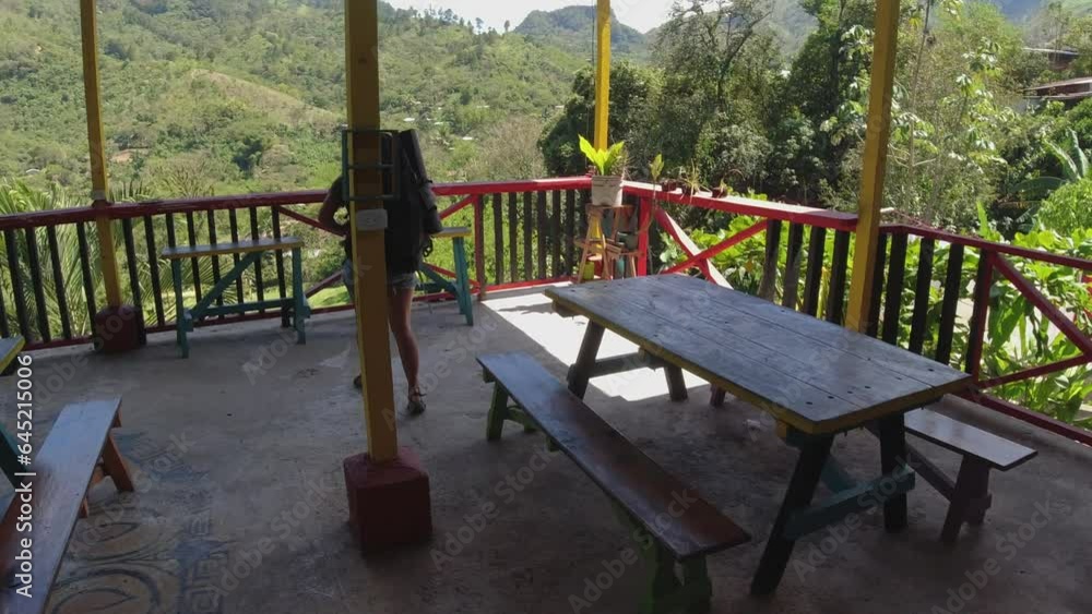 Latina with backpack walks to balcony rail at mountain jungle hostel Latina with backpack walks to balcony rail at mountain jungle hostel