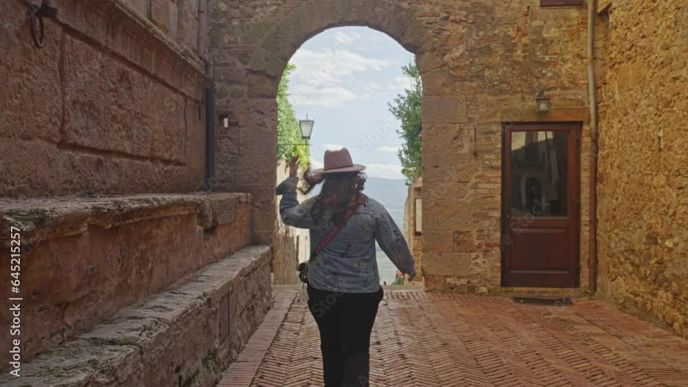 Female Tourist Walking Towards Archway In Pienza, Tuscany, Italy. following shot, back view Female Tourist Walking Towards Archway In Pienza, Tuscany, Italy. following shot, back view