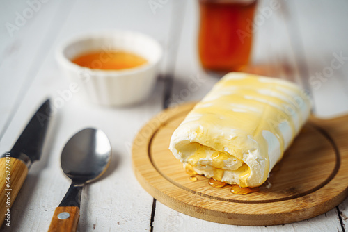 Close up picture of white cream milky kaymak butter roll poured with honey and tea on wooden plate. photo