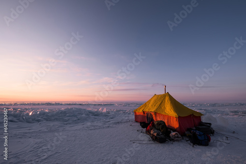 Orange Tourist Tent at sunrise on ice of winter lake Baikal. Winter trekking
