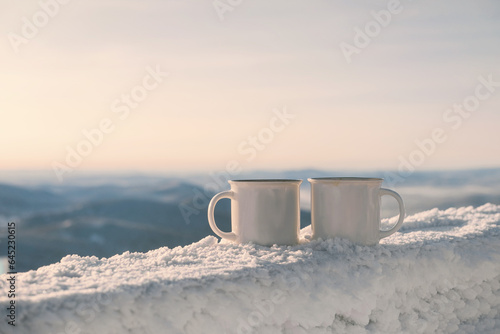 Hot drink in cups on frozen wooden table over winter mountains landscape
