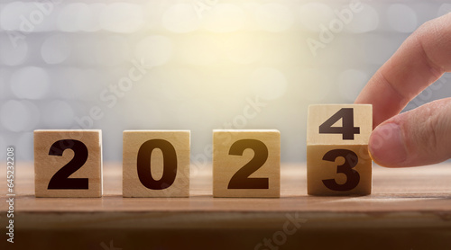 New year exchange concept. Man fingers with turning the calendar wooden block from 2023 to 2024. Figures of the year 2024 on a wooden block. Graphic banner work for the year ending and starting