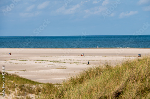 Strandk  be auf einem leeren Sandstrand im Vordergrund eine D  ne mit bilck   ber die Nordsee bis zum Horizont