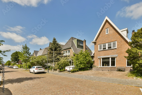 an empty street in the netherlands, with houses and cars parked on either sides there is a bright blue sky photo