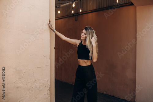 Beautiful blonde model woman, fashionable in a black suit, poses against the walls of a building