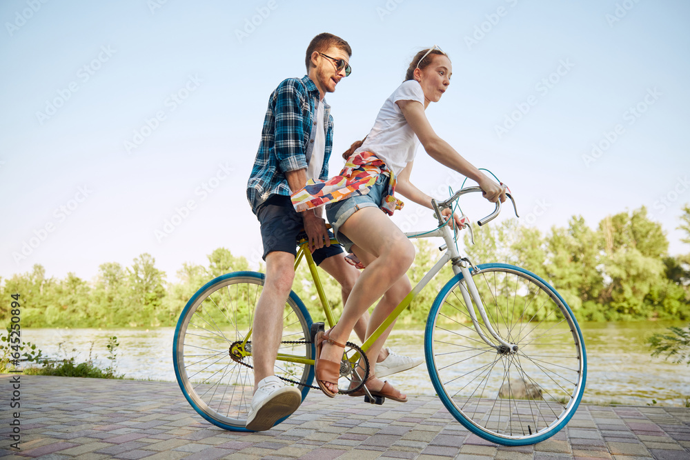 Bottom view portrait of young couple, woman and her boyfriend going for bike ride in river enbankment on summer day. Romantic date concept.