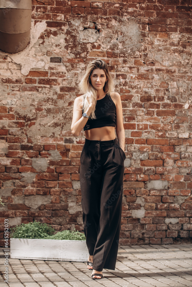Beautiful blonde model woman, fashionable in a black suit, poses against the walls of a building Beautiful blonde model woman, fashionable in a black suit, poses against the walls of a building
