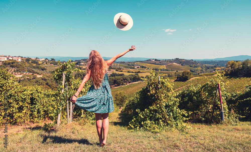 Fototapeta premium Happy woman tourist with blue dress and hat enjoying vineyards and winery in a valley- Chianty, Tuscany in Italy