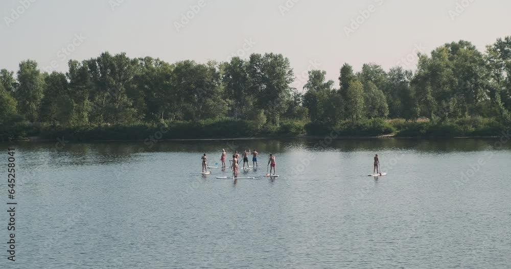 Sup board exercise. Group of students on river learn to swim on Sup board. Daytime, green trees, sky, calm water surface. Sup board exercise. Group of students on river learn to swim on Sup board. Daytime, green trees, sky, calm water surface.