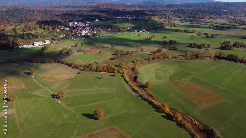 A wide-shot drone captures the picturesque small village surrounded by farms, fields, and autumnal forests, with visible plowed fields adding to the rural charm A wide-shot drone captures the picturesque small village surrounded by farms, fields, and autumnal forests, with visible plowed fields adding to the rural charm