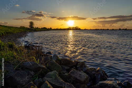 During this beautiful sunset, the stones on the banks of the river De Lek are just lit by the low sun