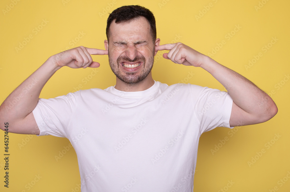 Man over yellow wall covering both ears with hands. Man over yellow wall covering both ears with hands.