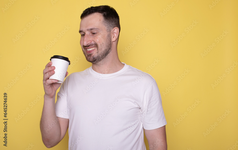 Young caucasian smiling bearded attractive man drinking hold paper cup of coffee isolated on yellow background studio portrait. People lifestyle concept. Young caucasian smiling bearded attractive man drinking hold paper cup of coffee isolated on yellow background studio portrait. People lifestyle concept.