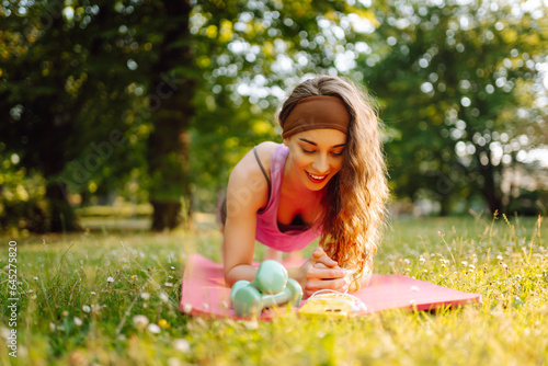 Fitness woman doing yoga, sports exercises in the park. Athletic woman sitting on a mat outdoors on a sunny lawn. Fitness. Active lifestyle. © maxbelchenko