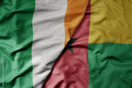 big waving national colorful flag of ireland and national flag of guinea bissau .