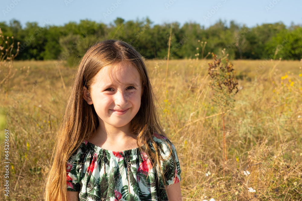 Portrait of a happy five-year-old girl in nature walking in the field in the summer.