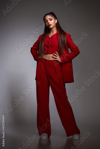 young brunette girl with exquisite beautiful makeup and neat hairstyle in a stylish red trouser suit posing in the studio