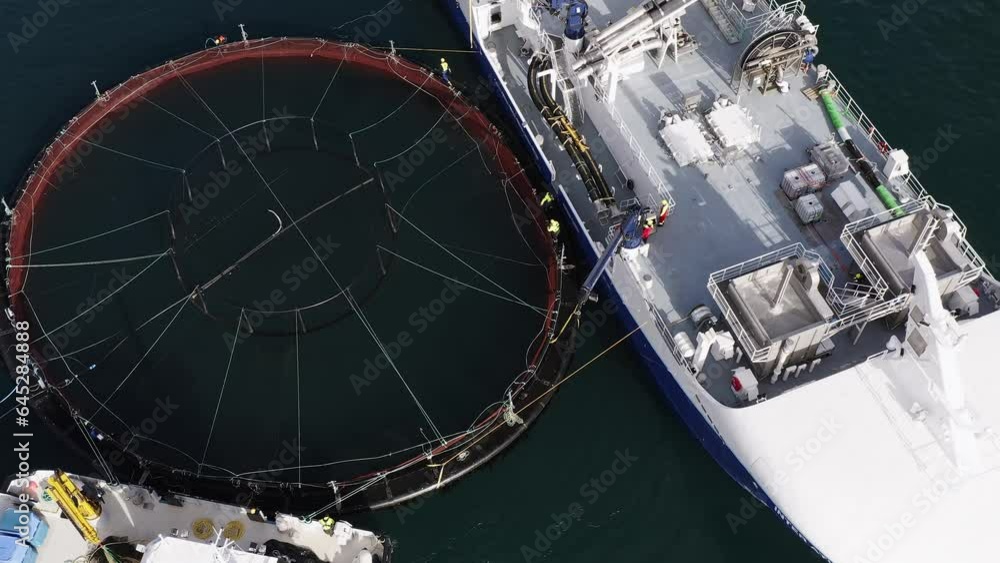 Drone shot of workers operating a crane by a pen on a fish farming vessel. Drone shot of workers operating a crane by a pen on a fish farming vessel.