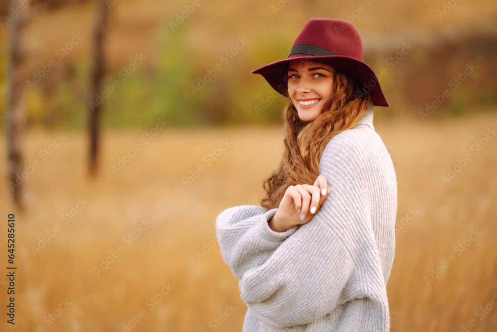 Smiling woman in a hat in an autumn meadow enjoying the weather, spending time outdoors. Lifestyle, relaxation and weekend concept.