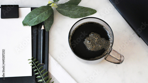 Above of Black Coffee Cup on White Desk with Blank Paper and Green Plant