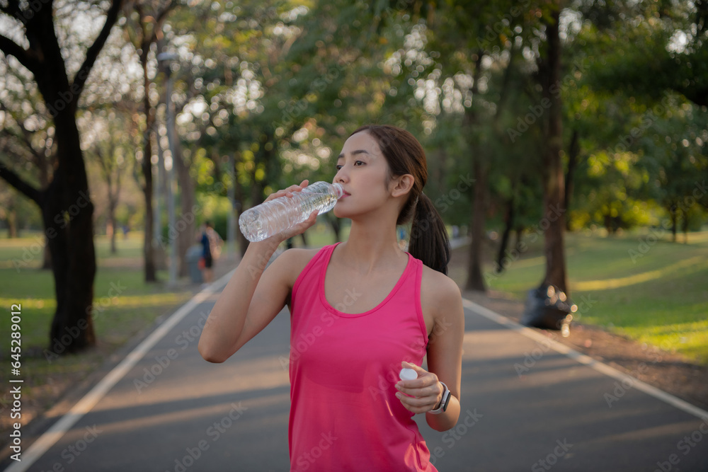 Asian woman resting after jogging. She is drinking water in the garden.