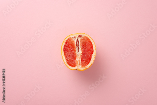 Sex ed symbolism. Top view perspective of grapefruit half, representing female anatomy, on pale pink surface with open area for text or advertisement