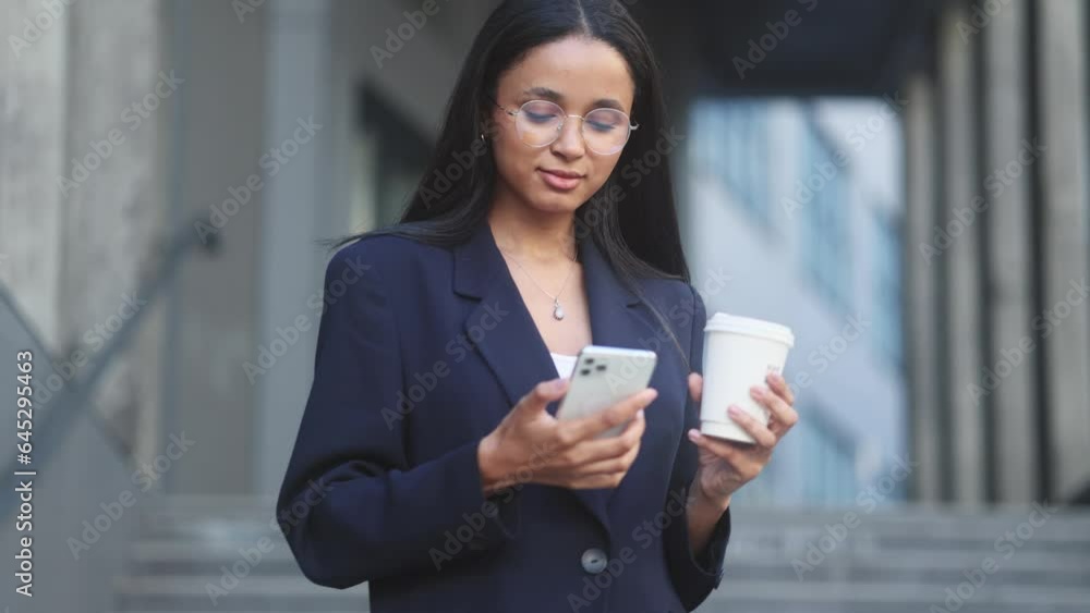Successful young businesswoman with cup of coffee hold smartphone scrolling social media texting browsing online checking email during break at work in modern business centre Successful young businesswoman with cup of coffee hold smartphone scrolling social media texting browsing online checking email during break at work in modern business centre