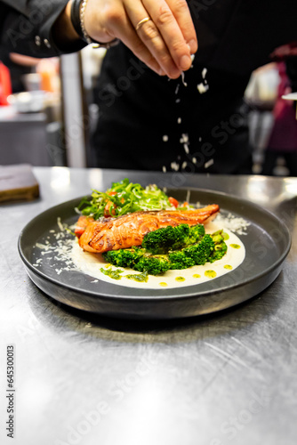 chef hand cooking salmon steak with broccoli and salad on restaurant kitchen