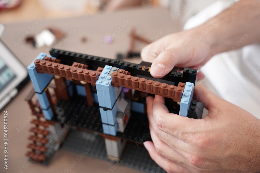 Naklejka premium lego medieval market village 1601, A person is building a lego house, lego village set at morning on table.
